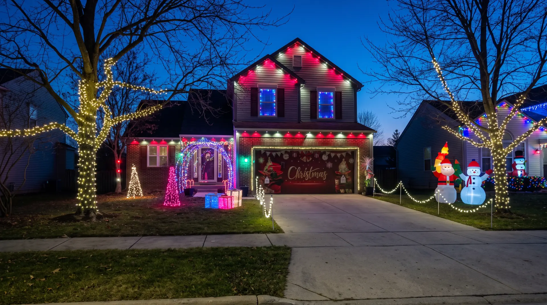 Two-story home with red and white roofline lights, wrapped trees, and full yard display
